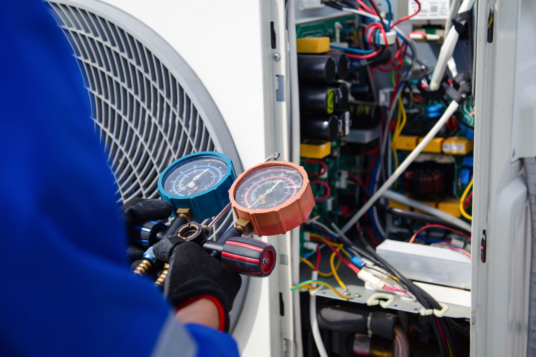Technician using gauges to check HVAC system pressure inside unit.