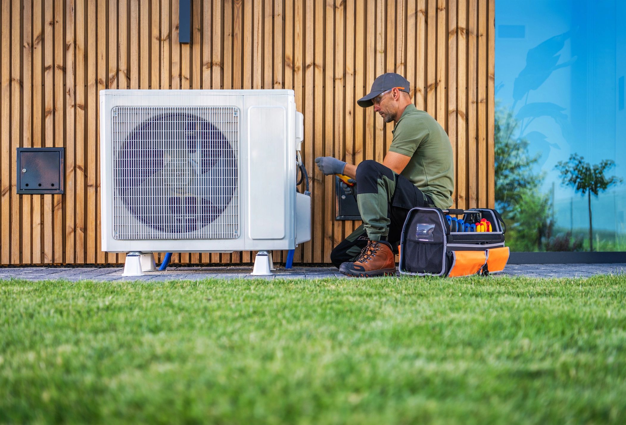 Technician repairing an outdoor air conditioning unit beside a wooden wall.