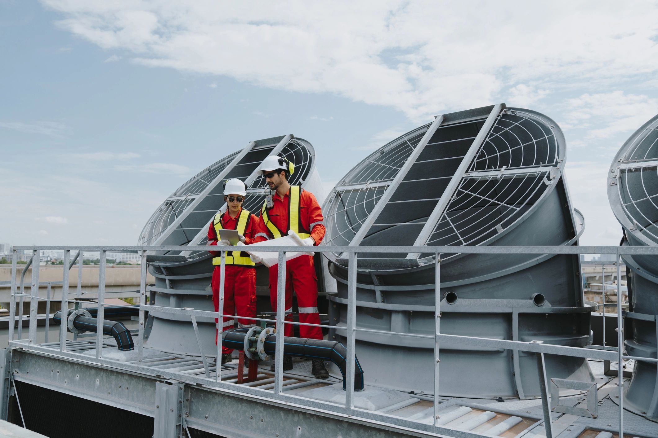 Two workers in red safety gear inspecting industrial equipment outdoors.